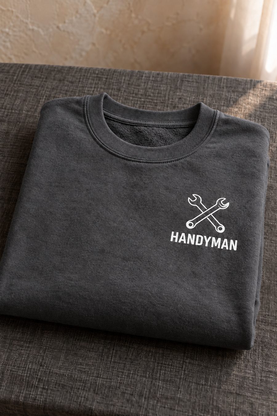 A folded charcoal sweatshirt with crossed wrenches and the word HANDYMAN printed in white on the chest.