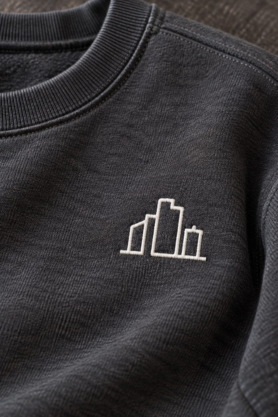 A building icon embroidered in white thread on the chest of a charcoal sweatshirt.